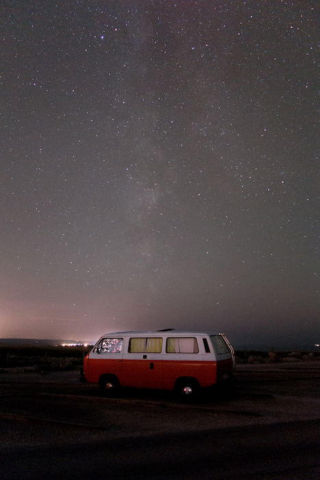 Image of a red camper van parked under an impressive starry sky
